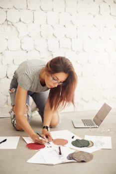 Female fashion design student drawing sketches and illustrations working on a laptop in a bright studio environment.